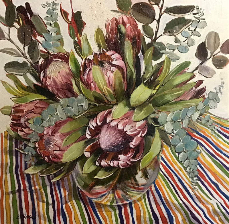 bold pink and red protea flowers and eucalyptus leaves in clear round vase on brightly striped cloth
